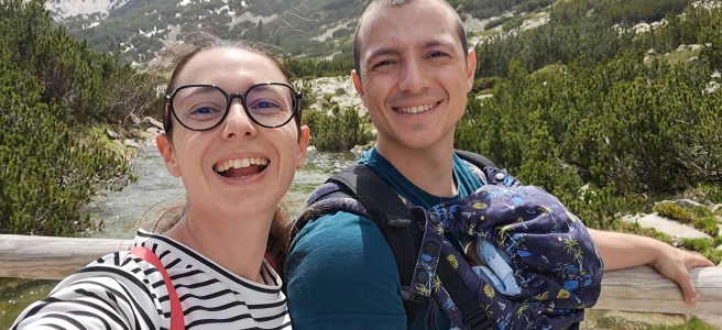 Млади майка и баща в планината с малко бебе в ергономична раница.